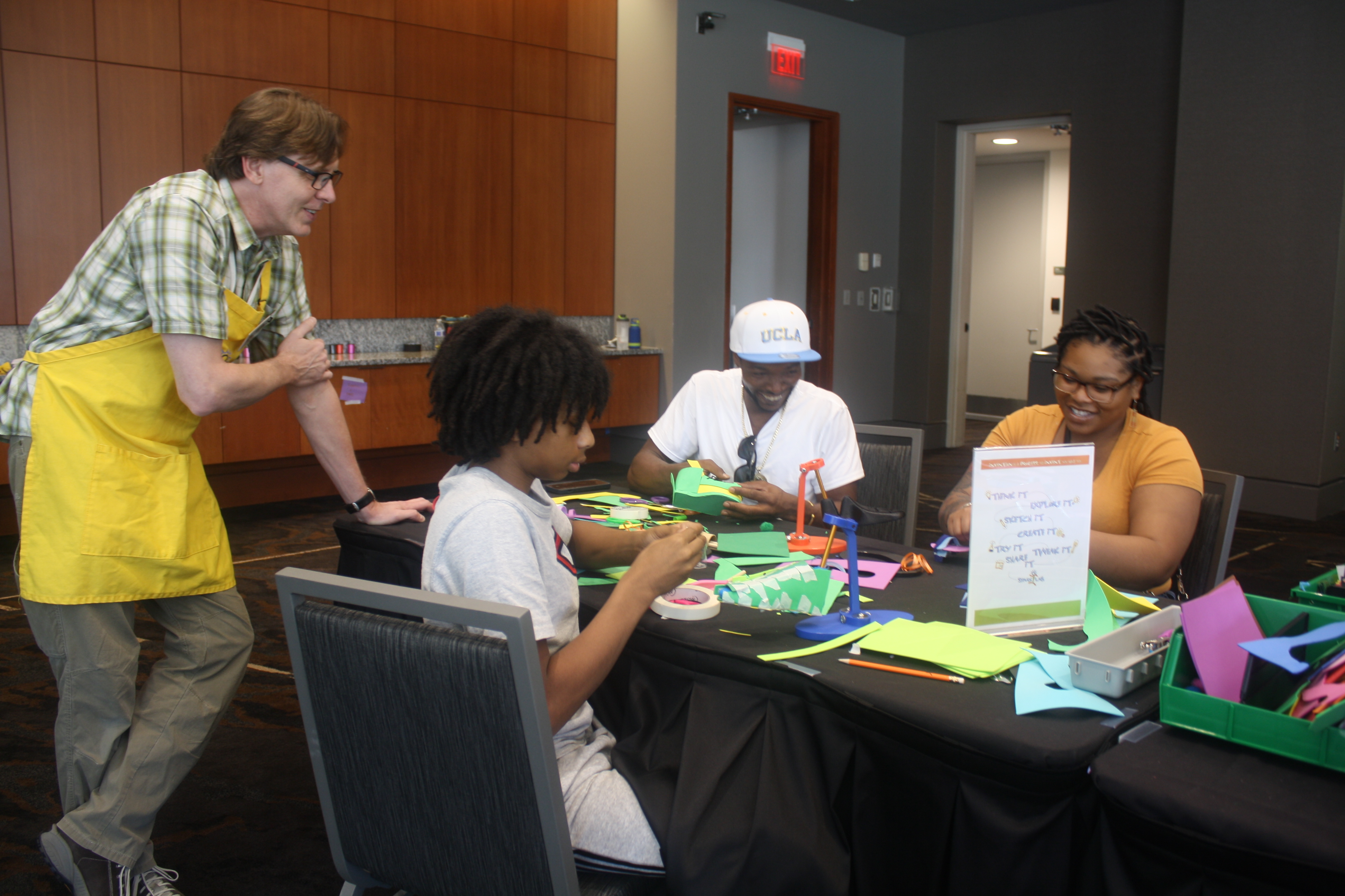 A family of three sits at a table and works on the Design a Shoe activity