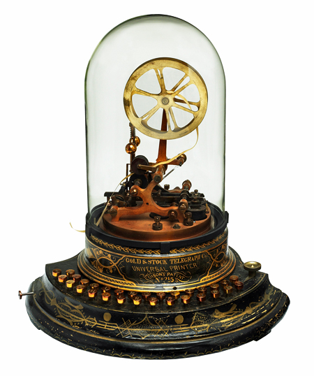 A round metal base with gold ornamentation holds 2 sets of keys, inscribed: Gold & Stock Telegraph Co., Universal Printer, Edison’s Patent, No. 215. A metal spool of paper tape sits atop the base and electromechanical contacts, covered by a glass dome.