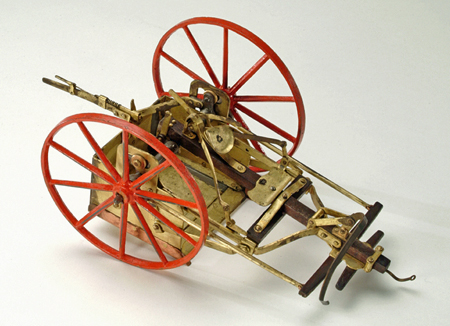 Metal and wood model of a wheeled, horse-drawn device to smooth road surfaces by scraping.