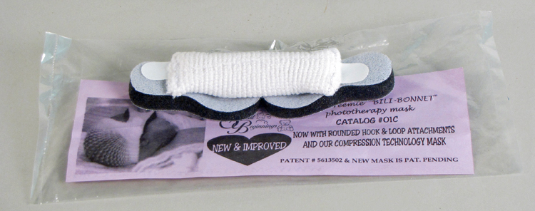 A small eye mask for an ultra-preemie baby. The mask is made of gray foam with Velcro tabs and a rolled up gauze bonnet.