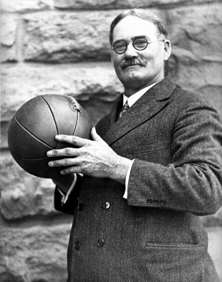 Three-quarter profile photo of James Naismith, wearing a suit and tie and holding a basketball.