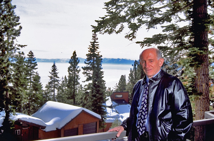 Jerome Lemelson standing on a deck overlooking snow-covered roofs and Lake Tahoe. He is smiling at the photographer.