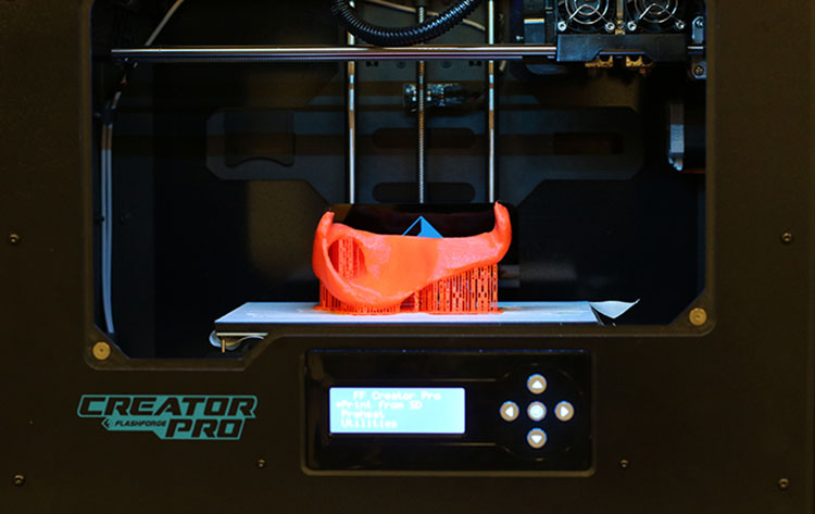A 3D printer with a partially completed bright orange racing glove