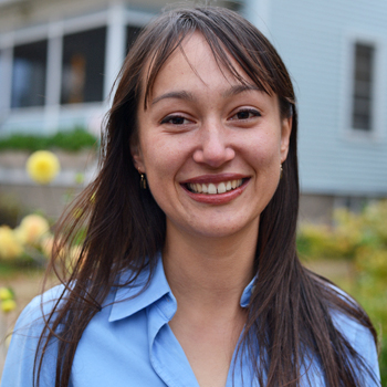 Headshot of 2017 Lemelson Fellow Spring Greeney. She was photographed outside, with flowers and a white house in the background.