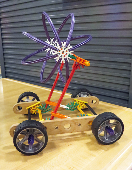 A child has built a model for his or her idea for a nuclear-powered car, using plastic wheels, wooden rails, plastic gears, and flexible plastic sticks. The top of the car looks like the symbol for nuclear power.