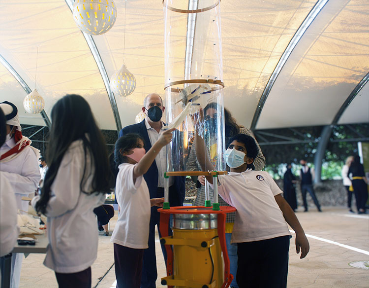 3 children test their inventions in the wind tunnel as 2 adults look on