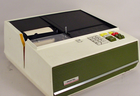 Rectangular black-and-beige plastic box with keypad on right and register tape on left.