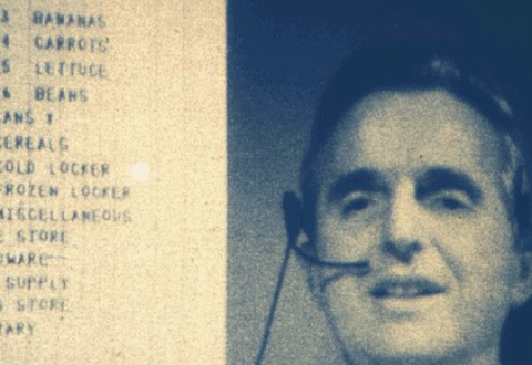 Screenshot of Douglas Engelbart presenting the mother of all demos on 9 December 1968. Engelbart wears a headset and his head and shoulders appear on the right side of the screen. Part of a shopping list, including grocery items bananas, carrots, lettuce, beans, and more, is on the left side. 