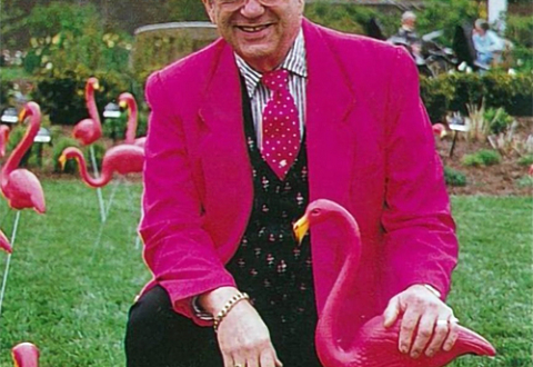 Don Featherstone posing with plastic pink flamingos on a lawn