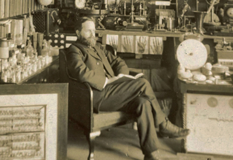 William J. Hammer seated among his large collection of scientific and experimental apparatus