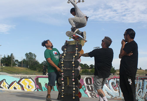 A skater in mid-air jumping over 13 skateboards stacked on horizontal edge