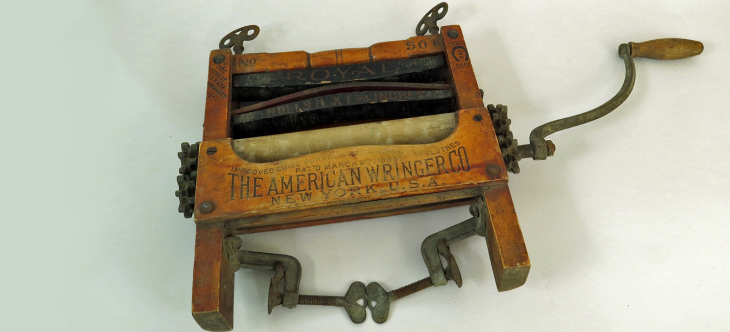 Color photo of a clothes wringer, comprised of two rubber rollers in a wood frame with metal gears, clamps, etc.