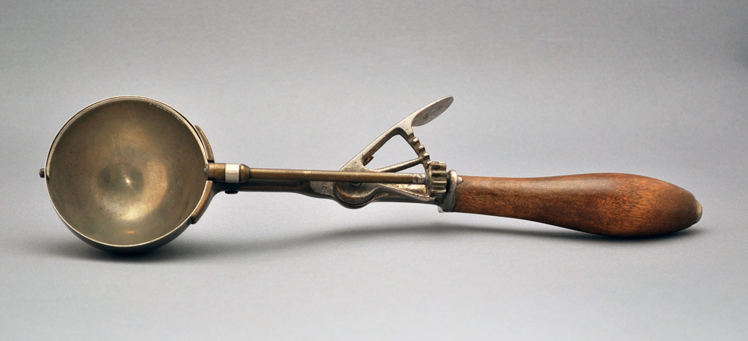 An ice cream scoop laying on its side, with a metal bowl, wooden handle, and lever for releasing ice cream