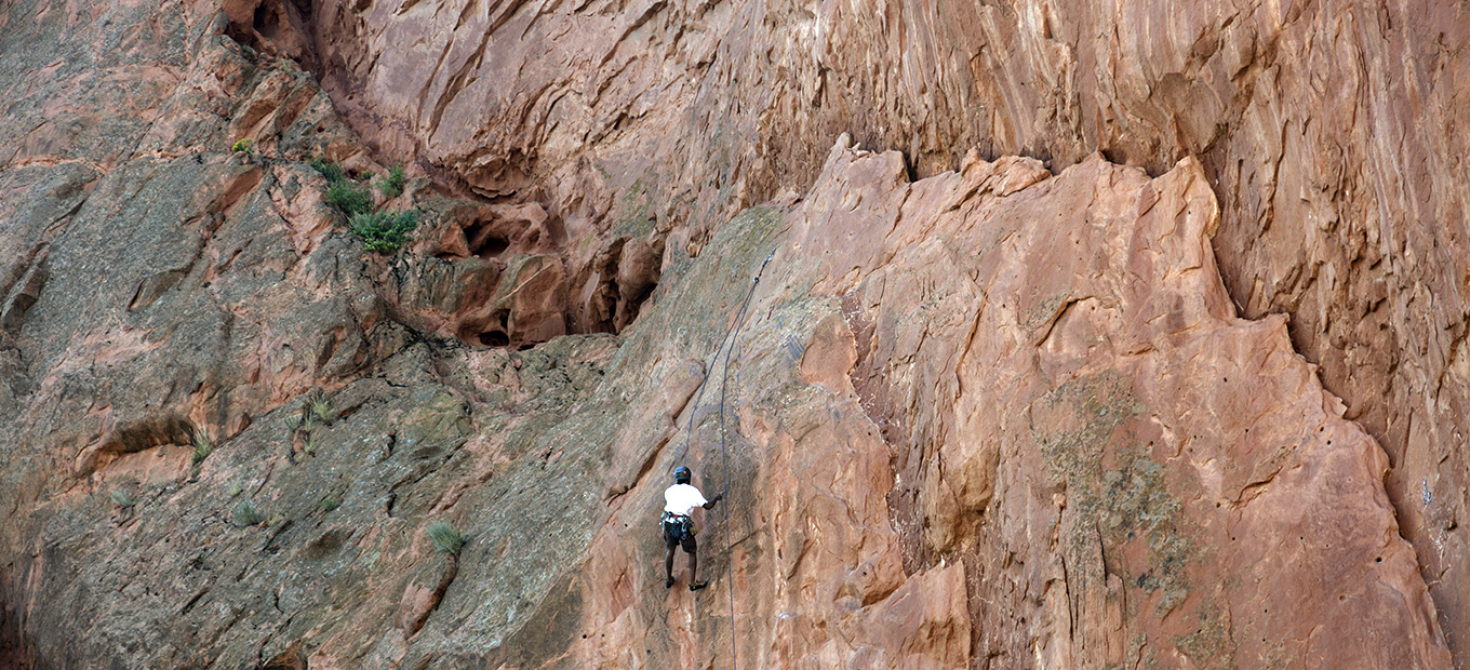 A lone rock climber scaling a red rock wall