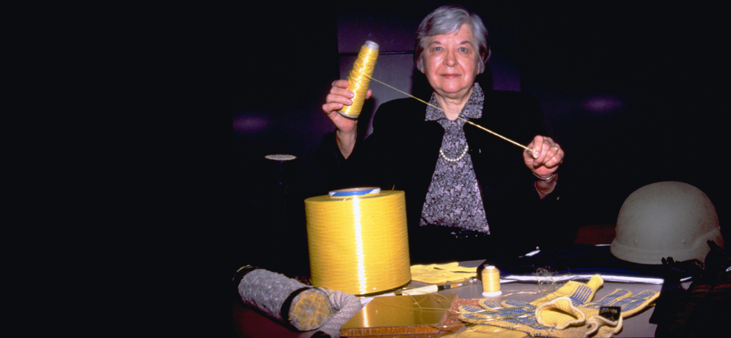 Stephanie Kwolek holding up a thread from a spool of Kevlar