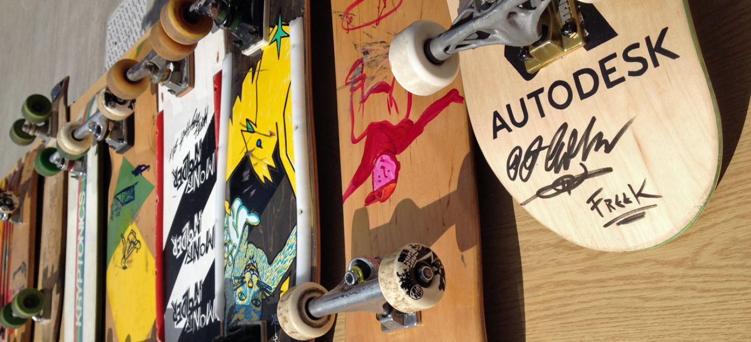 A row of 8 skateboards, deck down, showing the addition of artwork over time; the oldest boards are plain wood.