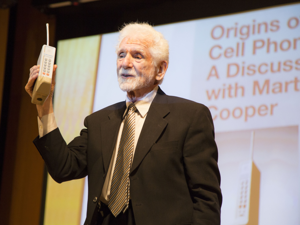 Martin Cooper holds up an early &quot;brick&quot; cell phone.