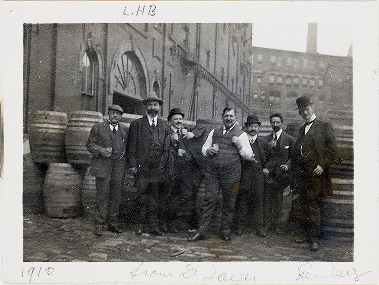 Seven men in suits standing for a photo in from of wooden barrels. In pencil under the photo is written: &quot;From Dr. Jaeger&quot;