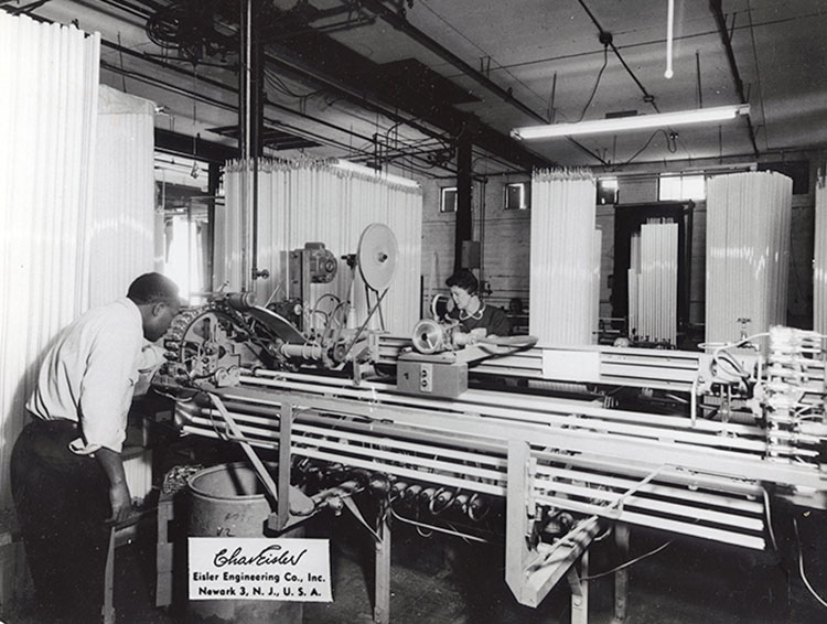 A man and a woman inspecting or making long glass tubes