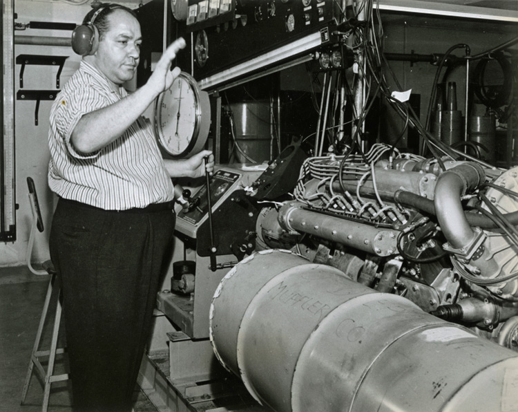 Andy Granatelli, wearing hearing protection, in front of a large engine.