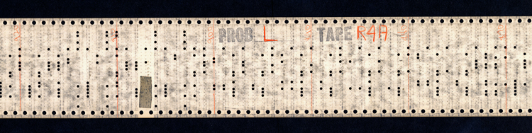 A long strip of paper, about 3 inches wide. The upper and lower edges have regular rows of perforations. The center of the tape has punch holes carrying the program code. The words “Prob L” and “Tape R4A” are stamped at the top of the strip, and regularly-spaced red vertical lines have been drawn across the tape and numbered 870, 880, 890, 900, 910, and 920.