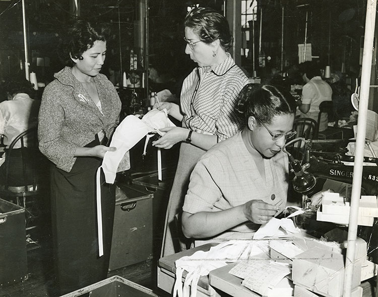 Two women inspecting a bra while a third sews