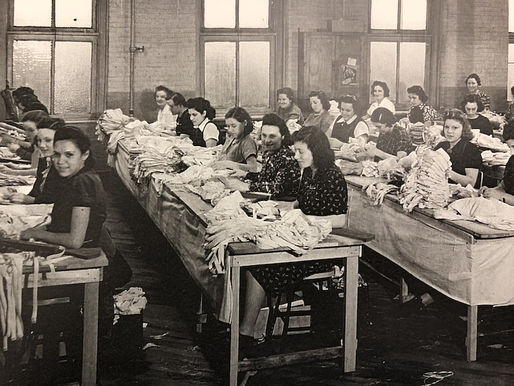 Dozens of women sitting at long tables working on bras