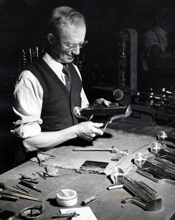 Charles Brannock holding a Brannock foot measuring device at his workbench