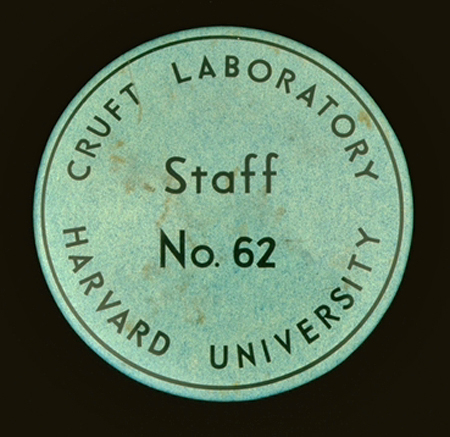 A round green metal badge, about 1.5 inches in diameter. The words “Cruft Laboratory Harvard University” are printed around the outer edge, and the words “Staff No. 62” are printed in the center of the badge.