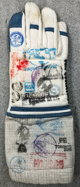 Fencing glove worn by Ibtihaj Muhammad during the 2016 Rio Olympic Games . The glove is white and blue and made of 50% Kevlar, 25% metal, and 25% cotton. The glove has suede leather palms and fingers for added protection and Velcro at the cuff to secure the glove to the wrist. There are multi-colored stamps throughout the surface. 