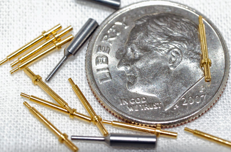 13 small specialty pins made by W.H. Bagshaw Co. in a random arrangement and photographed with a dime for scale