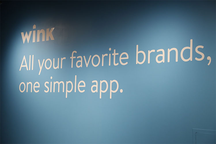 Wink brand logo painted on a wall with the tagline, &quot;All your favorite brands, on one simple app.&quot;