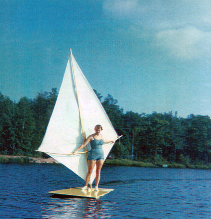 A woman rides a sailboard (or windsurfer) invented by Newman Darby