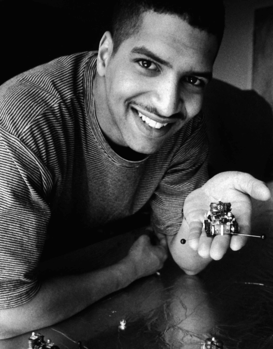 A young Black man holding a tiny robot on his palm