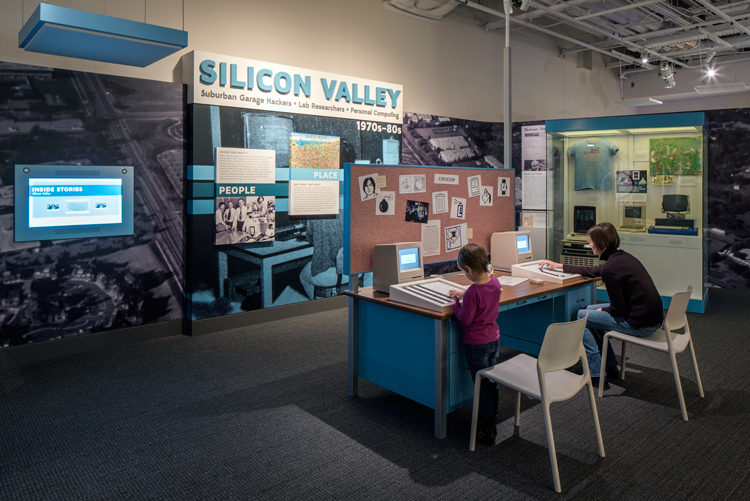 A child and a woman are working on the make-an-icon interactive in the Silicon Valley section of Places of Invention. They turn over black-or-white tiles that represent pixels to design computer icons.