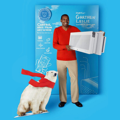 Advertising image showing inventor Garthen Leslie holding the Aros air conditioner that he invented. He stands against a backdrop of blueprint-type sketches for the air conditioner. A cut-out of a polar bear wearing a red scarf is at his feet.