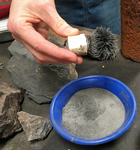 Close-up of David Stone's hand holding a small magnet covered in steel dust. The particles are so aligned as to give the appearance of a shaving brush.