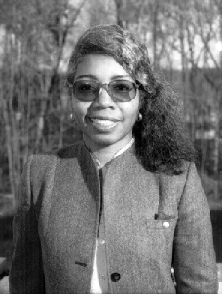 Informal portrait photo of Valerie L. Thomas, 1995. She is standing outside, with trees in the background. She is wearing tinted glasses and an unbuttoned jacket.