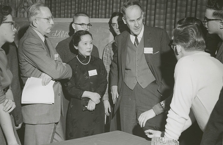 Chien-Shiung Wu standing in a group of 8 other people who are listening to a conversation between 2 of the men