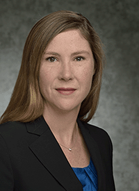 Headshot of a white woman with long blonde hair against a gray background.