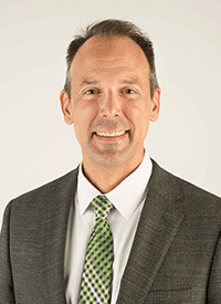 Headshot of a white man in professional dress in front of a light colored background.