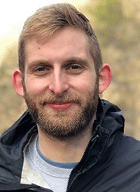 Headshot of a white man with blonde hair and a beard, taken outside.