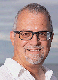 Headshot of a white man with glasses and gray hair and gray short beard, taken outside.