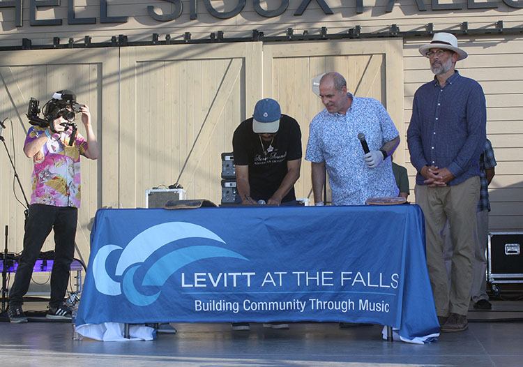 A man signing a paper at an outdoor table while 2 other men look on