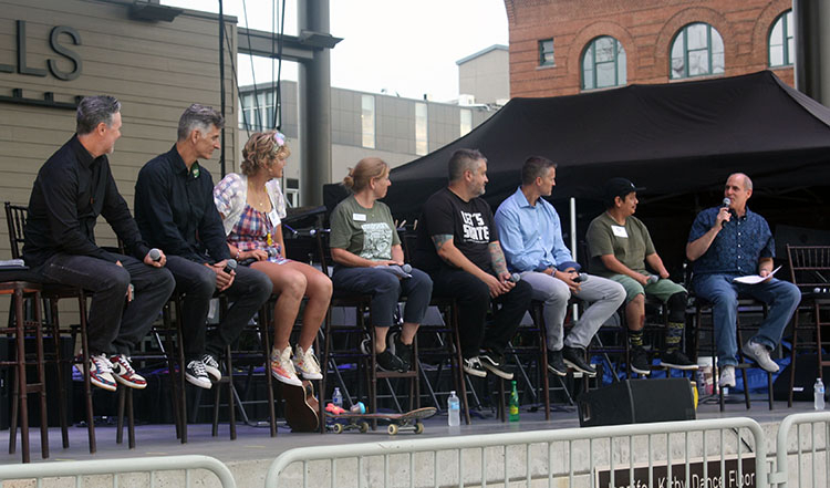 A line of 8 people sitting on tall stools on stage having a discussion