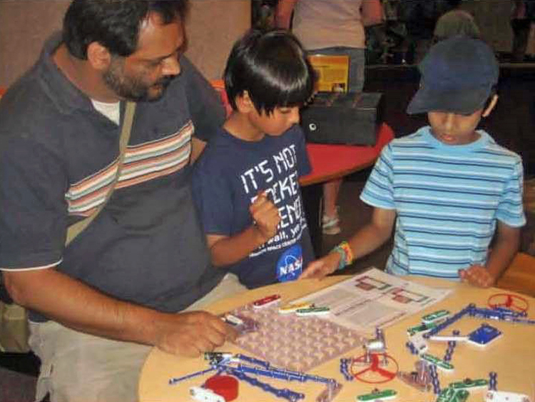 An adult man and two young boys working at a table on a snap circuits activity in Spark!Lab.