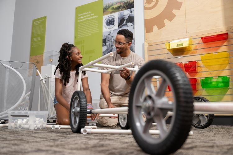 Two visitors to SparkLab in Conner Prairie work together assembling a vehicle made from white tubes.