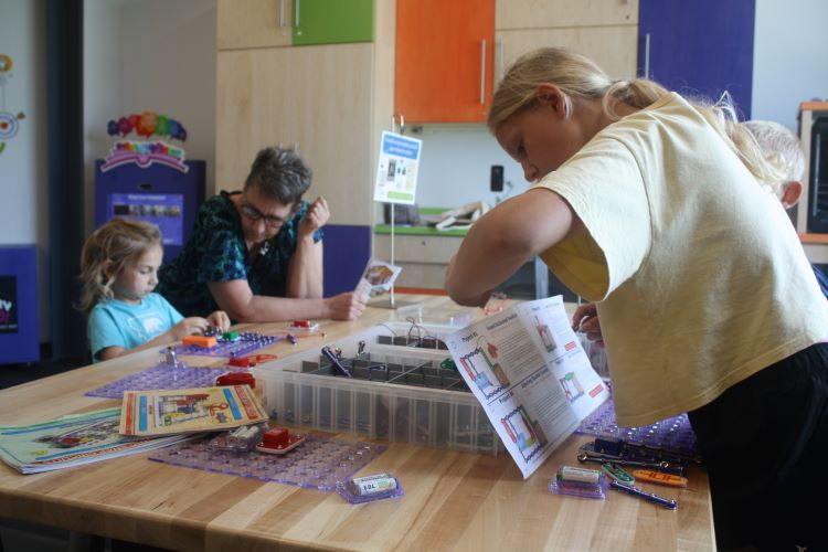 Two young inventors and a grown-up work independently at a table with the snap circuit activity.