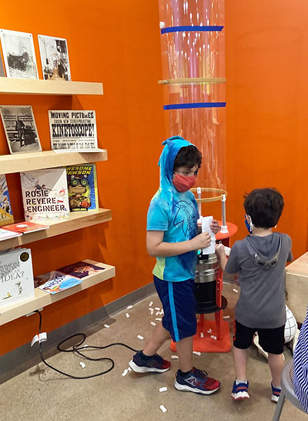 2 young boys in front of a plastic vertical wind tunnel