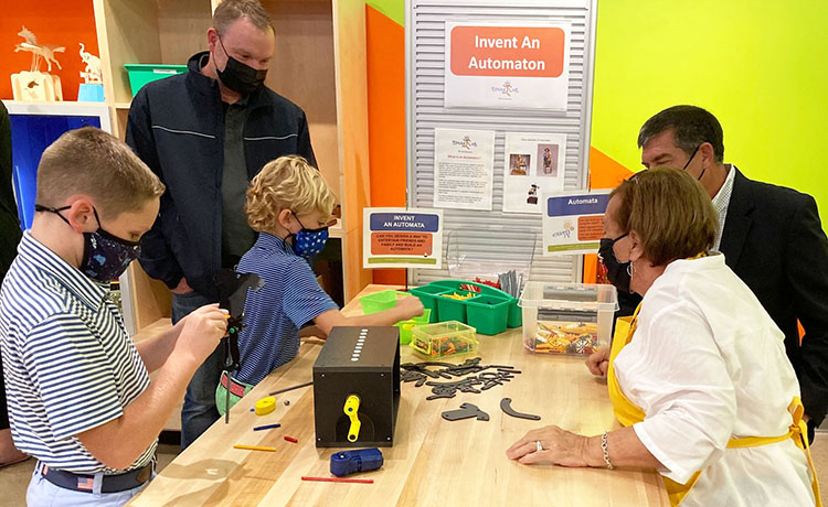 2 young boys, 2 adult men, and a woman facilitator work on inventing an automaton